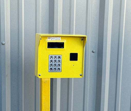 A yellow box with a keypad and a small screen is mounted on a metal pole.