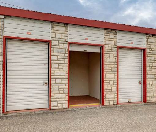A building with red trim and a red roof has three garage doors.