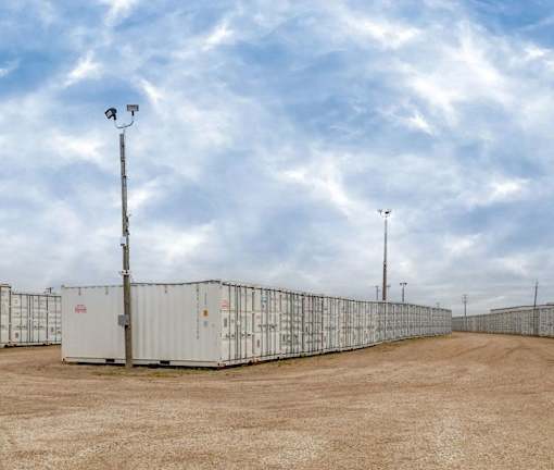A row of white shipping containers are lined up in a field.