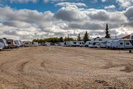 a row of rvs parked in a dirt lot with clouds in the sky