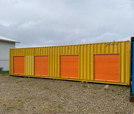 A yellow container with orange doors is parked in a gravel lot.