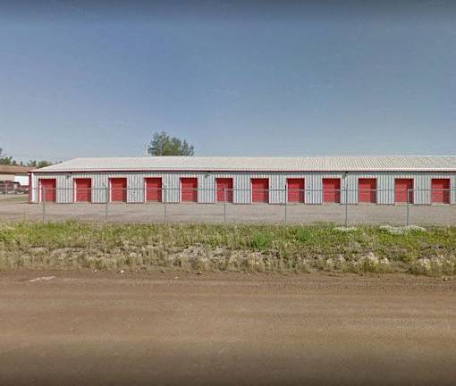 A long building with red doors is surrounded by a fence.