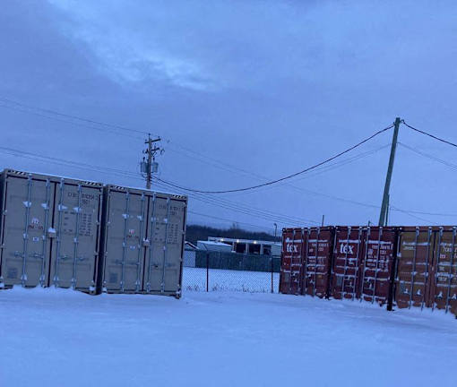 A row of shipping containers are lined up in the snow.