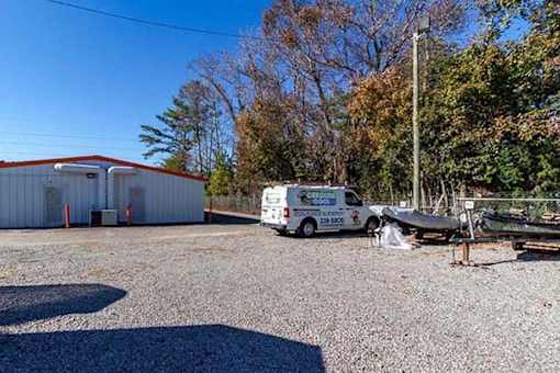 A white van is parked in front of a white building with a boat on the ground.