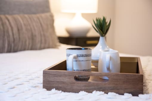 a tray with coffee cups and a vase on a bed