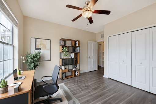 A room with a desk, chair, and a ceiling fan.