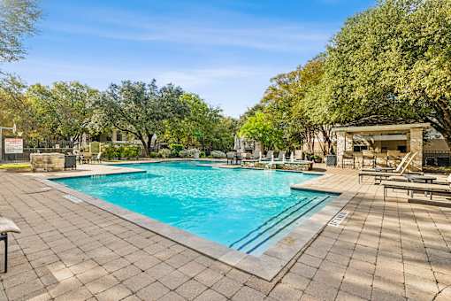 A large outdoor swimming pool surrounded by trees and a patio area with sun loungers.