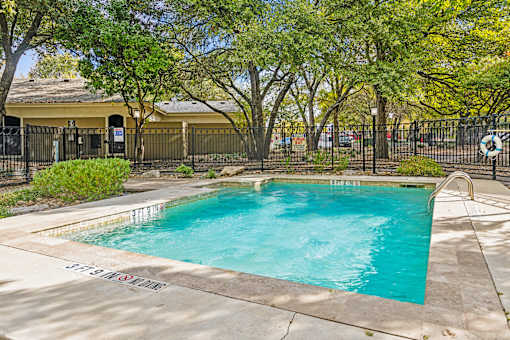 A small pool surrounded by trees and a fence.