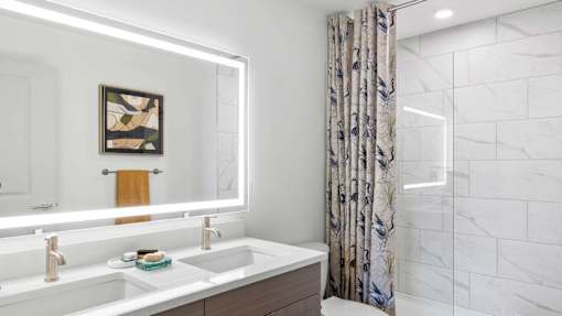 A bathroom with a marble wall and a floral shower curtain. at Lucie at Tradition Apartments, Port St. Lucie