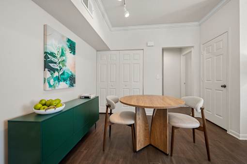 A green cabinet with a bowl of fruit on top and a painting of green leaves on the wall.