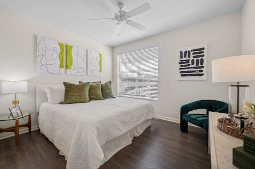 A bedroom with a bed, chair, and artwork on the wall.