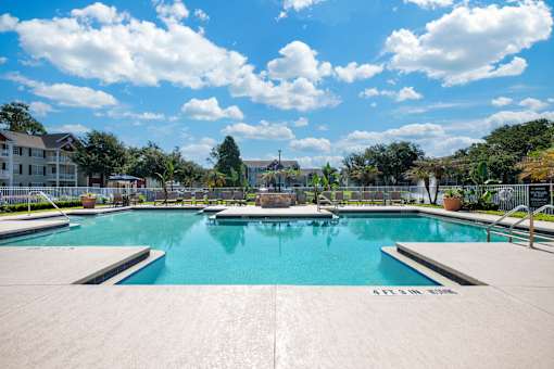 A large outdoor swimming pool surrounded by a concrete patio and a fence.