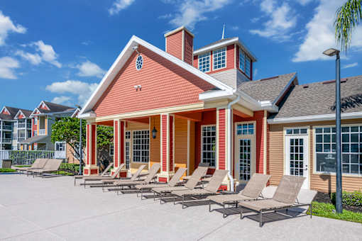 A red brick house with a porch and lounge chairs in front.