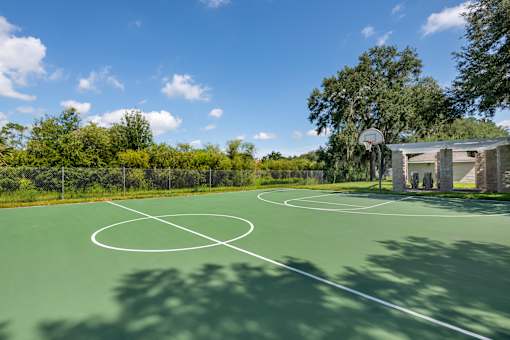 A basketball court surrounded by trees and a building in the background.