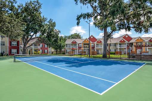 A tennis court is surrounded by apartment buildings.