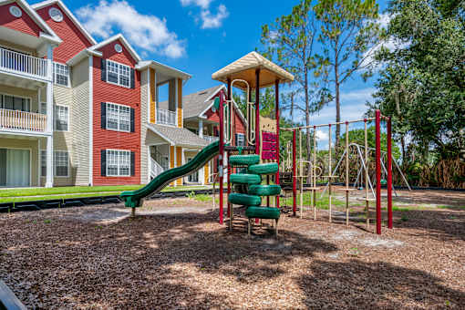 A playground with a green slide and red and white buildings in the background.