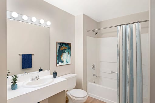 A bathroom with a white sink, vanity, toilet, and bathtub/shower