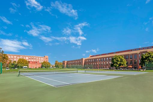 A tennis court is surrounded by a green fence and a brick building.