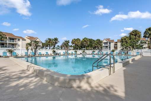 A large outdoor swimming pool surrounded by palm trees and lounge chairs.