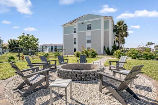 A fire pit surrounded by chairs in a gravel area.