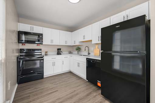 A black fridge in a kitchen with white cabinets.