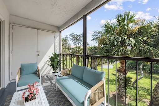 A balcony with a sofa, chair, and table with flowers.
