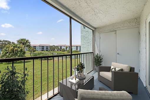 A balcony with a couch, chair, and table with a view of apartment buildings.