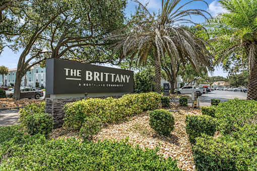 A sign that says "The Brittany" in front of a landscaped area.
