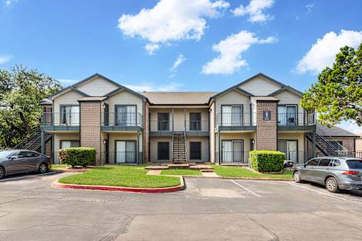 A sunny day at a two-story apartment complex with cars parked in the driveway.