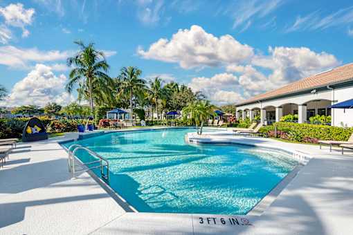 A large outdoor swimming pool with lounge chairs and an adjacent clubhouse overlooking a body of water