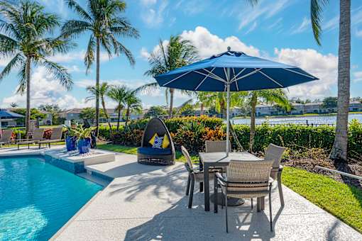 A poolside area with a table and chairs under an umbrella.