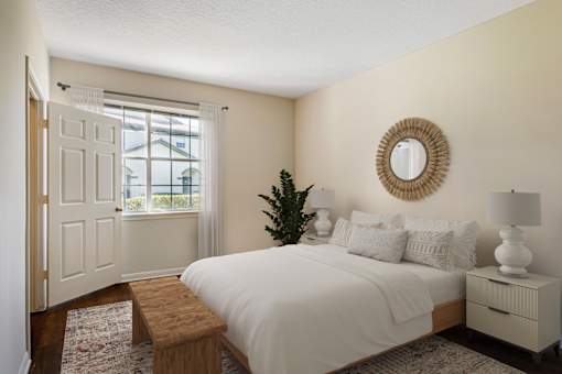 A bedroom with a white bed, a wooden bench, and a round mirror on the wall.