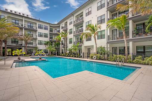 A swimming pool in front of a building with palm trees.