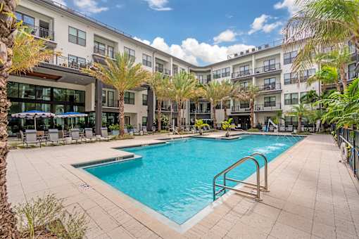 A swimming pool surrounded by palm trees and a building in the background.