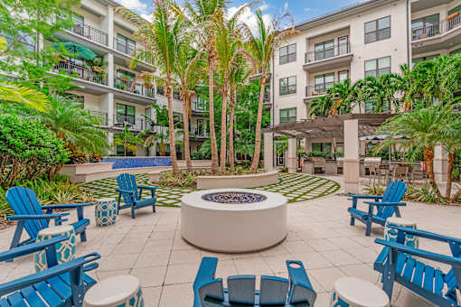 A patio with blue chairs and a fire pit in front of a building with balconies.