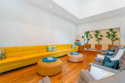 A living room with a yellow couch and a round ottoman.