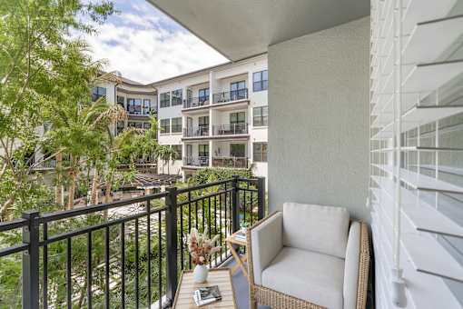 A balcony with a chair and a table with a vase of flowers on it.