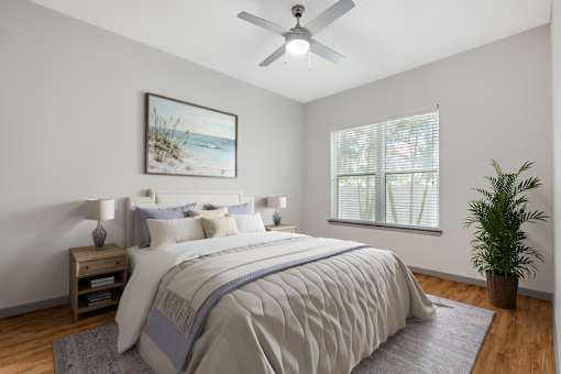 A bedroom with a large bed, a ceiling fan, and a potted plant.