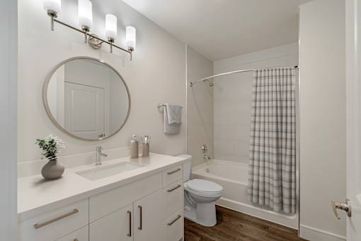 A white bathroom with a round mirror and a white toilet.
