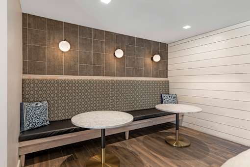 A modern lounge area with a bench, two tables, and wall lights.