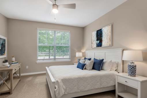 A bedroom with a large bed, a ceiling fan, and a window with blinds.