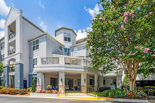 A large white building with a balcony and a tree in front.