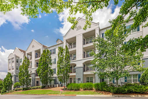 A large white apartment building with balconies and trees in front.