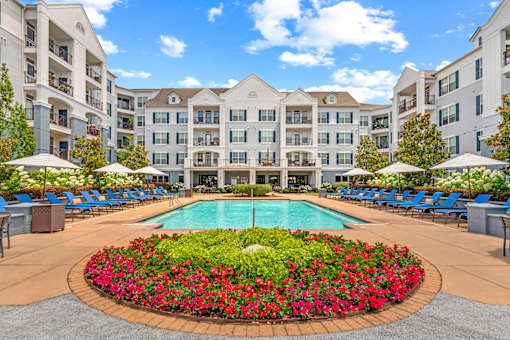 A large pool surrounded by a flower bed in front of apartment buildings.