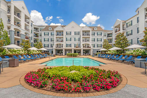A large pool surrounded by a flower bed in front of apartment buildings.