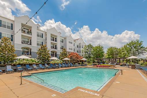 A large swimming pool in front of a white building with lounge chairs around it.