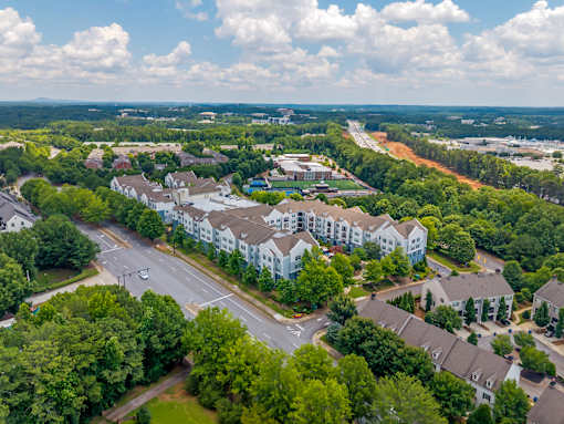 A large white building is surrounded by trees and a road.