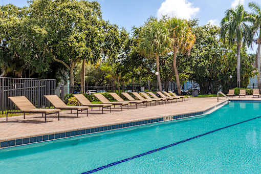 A pool surrounded by trees and lounge chairs.