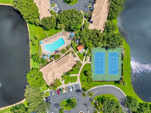 A bird's eye view of a park with a tennis court, a swimming pool, and a parking lot.