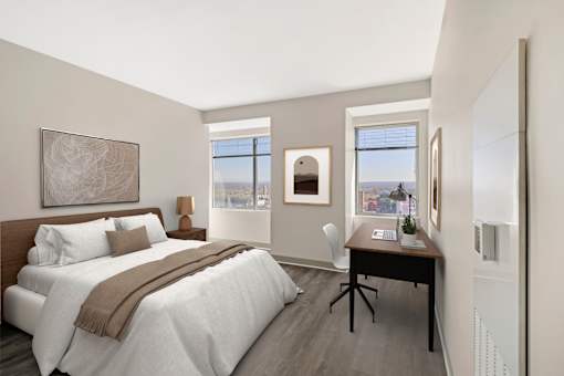 A bedroom with a large bed and two windows looking out to the city landscape